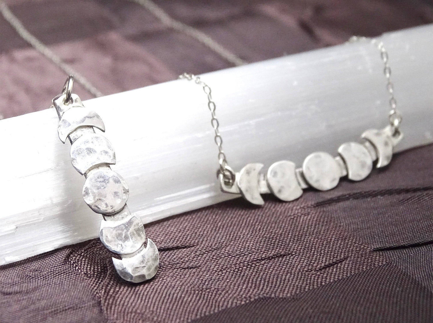 Brightly lit moon phase necklaces in vertical and horizontal designs, handcrafted in sterling silver with celestial theme.