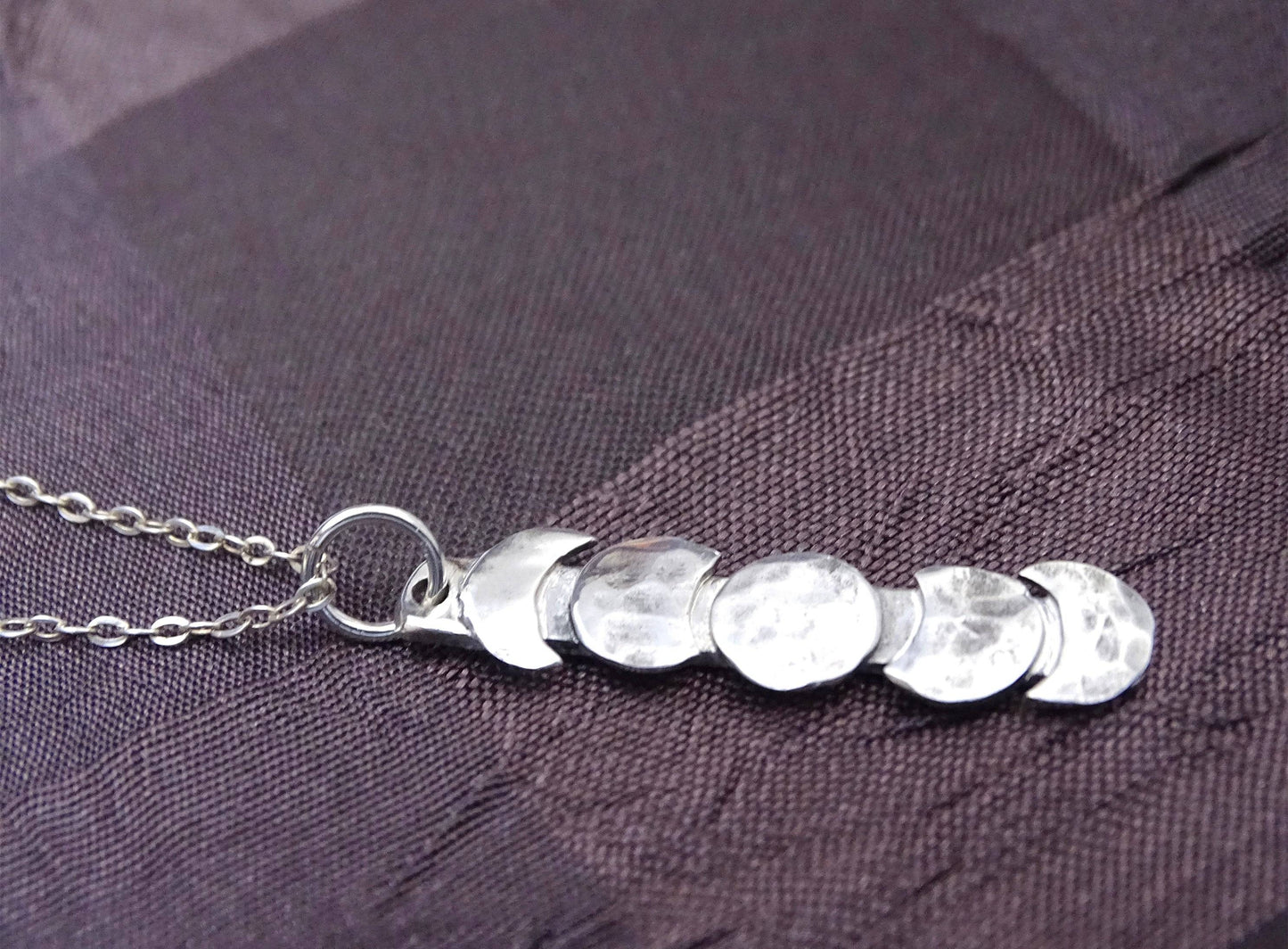 Close-up of vertical moon phase necklace in hammered sterling silver, showcasing lunar cycle design on fine silver chain.