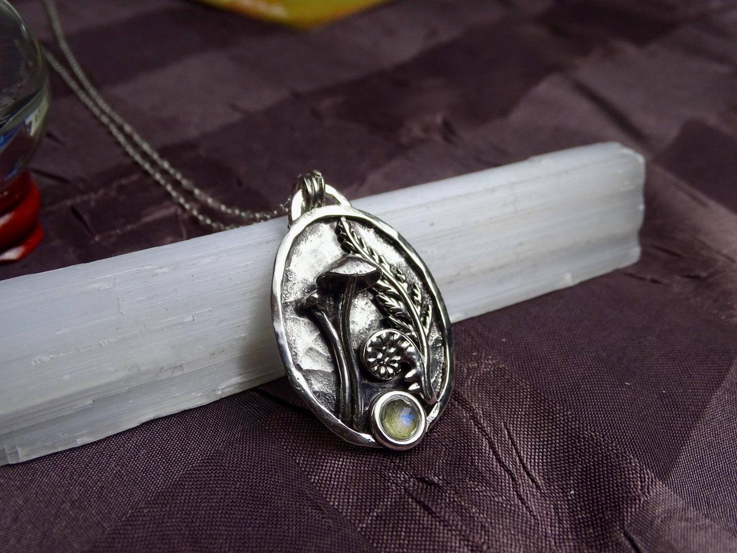 Close-up of sterling silver mushroom and fern pendant with labradorite gemstone, resting on a white crystal wand, ideal for nature-inspired gifts.