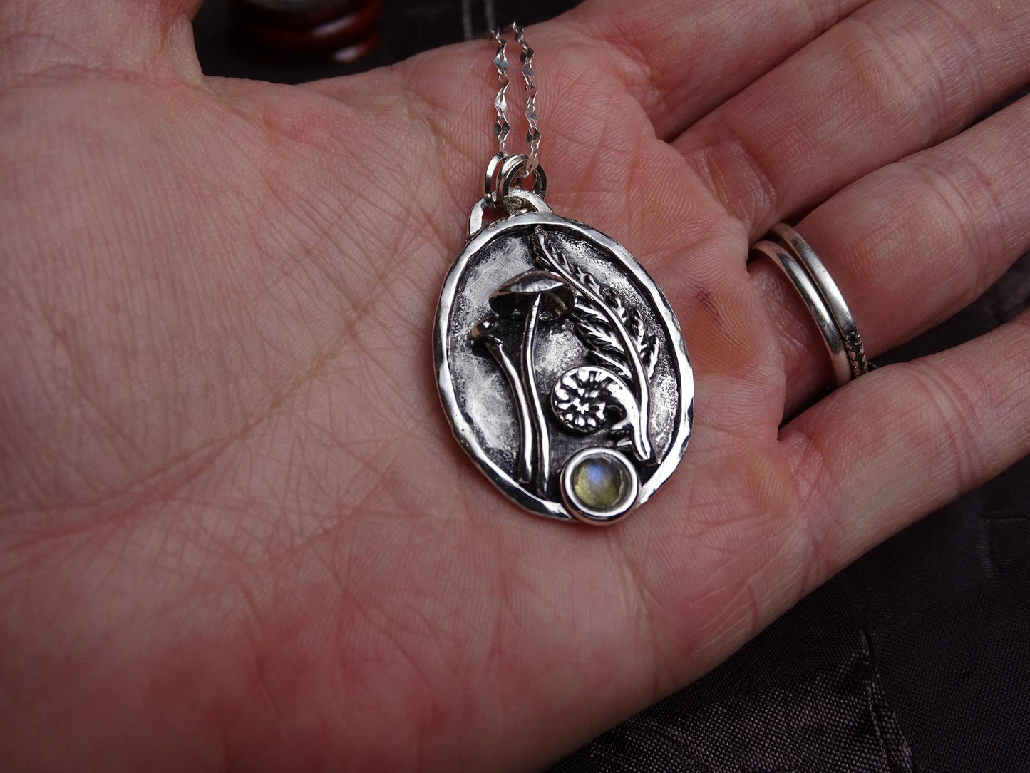 Sterling silver mushroom and fern pendant with labradorite gemstone shown in hand for size reference, highlighting handcrafted detail and texture.