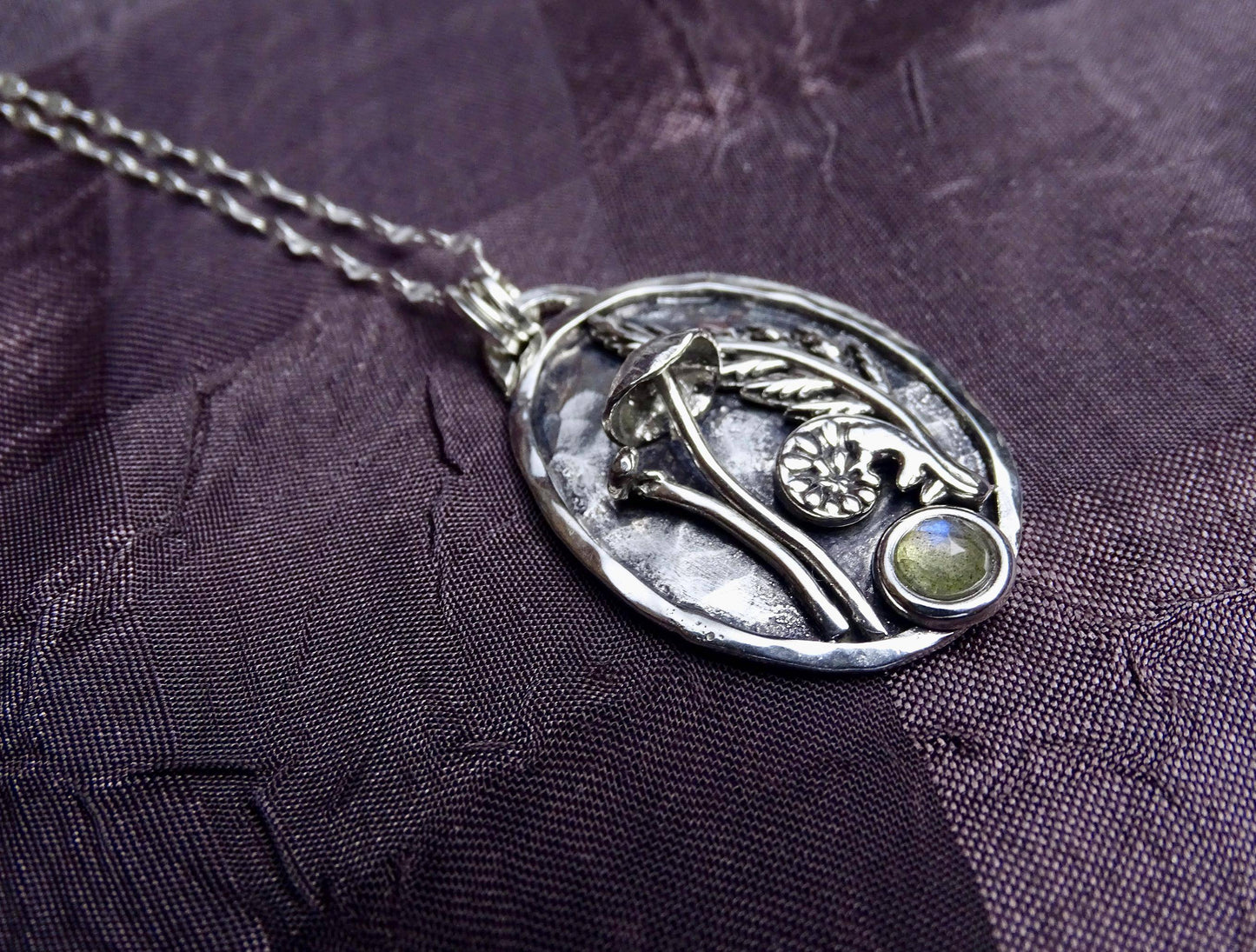 Angled view of sterling silver mushroom pendant with fern and labradorite, showcasing its handcrafted texture and organic design elements.