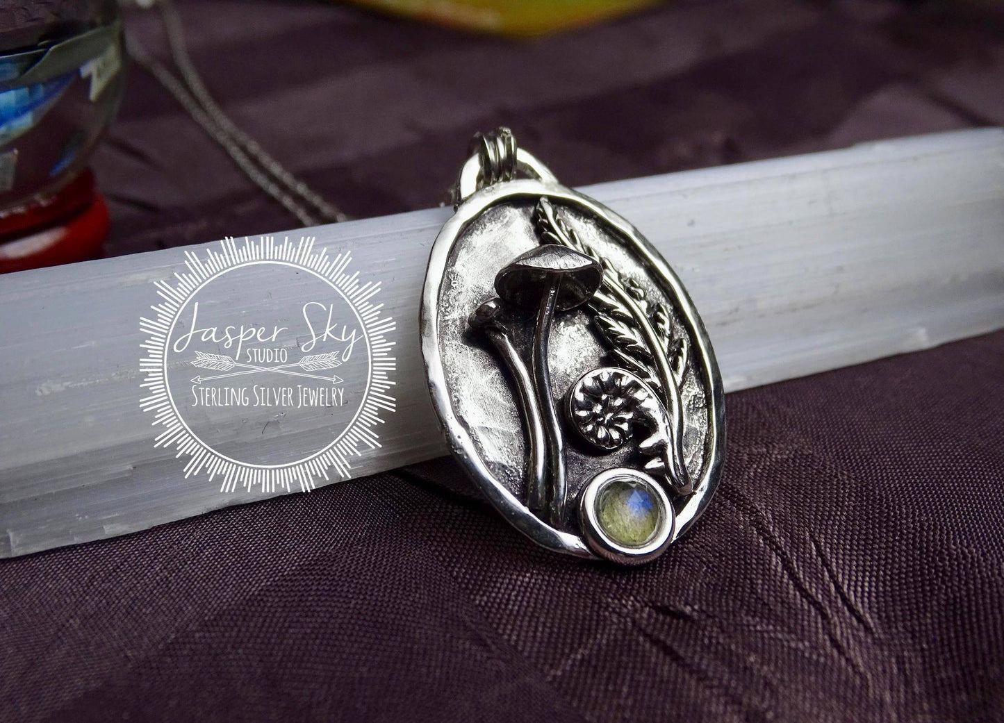 Sterling silver pendant featuring a mushroom, fern, and labradorite stone with textured background, symbolizing new beginnings and handcrafted artistry.