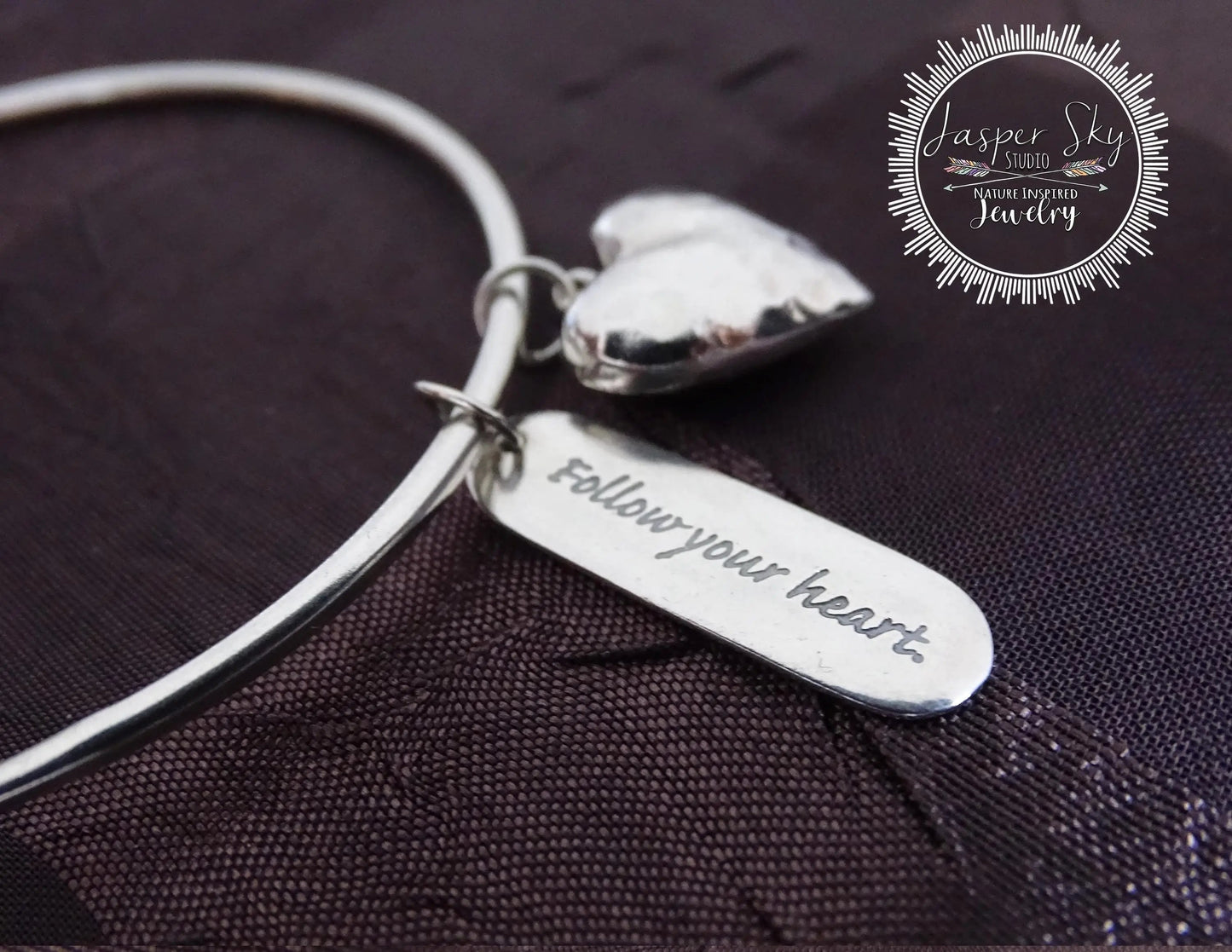 Close-up of sterling silver bangle bracelet featuring a heart charm and engraved inspirational message, perfect sentimental holiday gift.