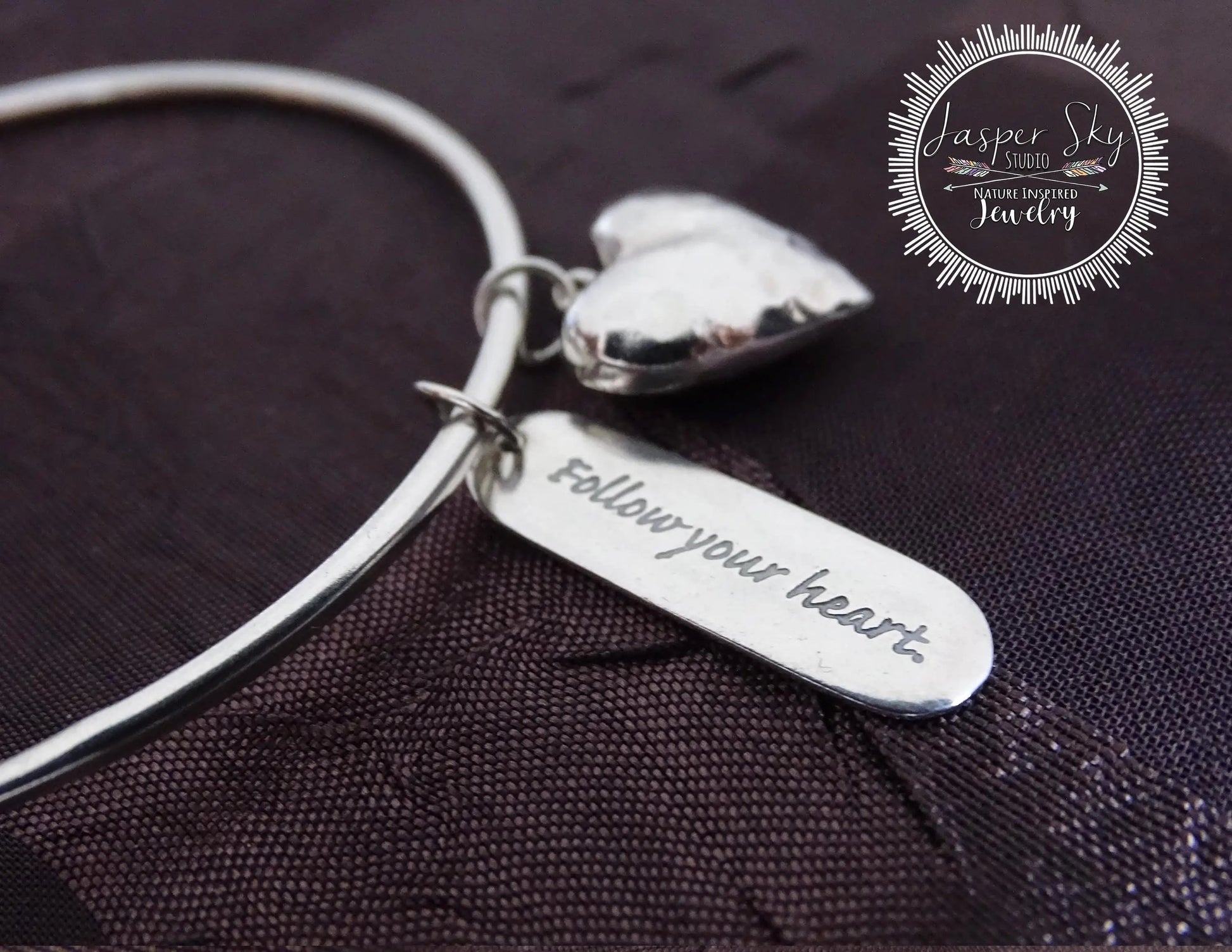 Close-up of sterling silver bangle bracelet featuring a heart charm and engraved inspirational message, perfect sentimental holiday gift.