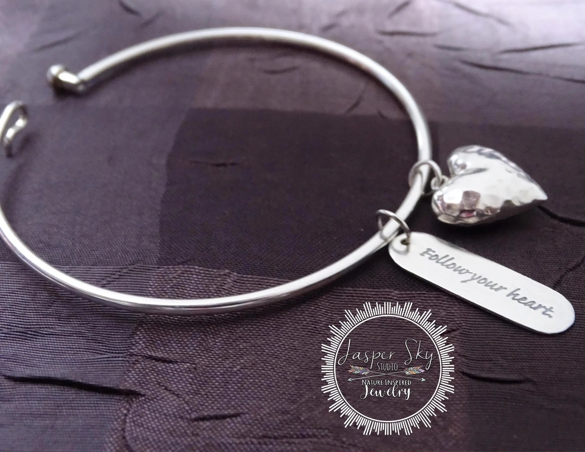 Elegant sterling silver bangle with heart and engraved charm reading 'Follow your heart,' a thoughtful and stylish holiday gift.