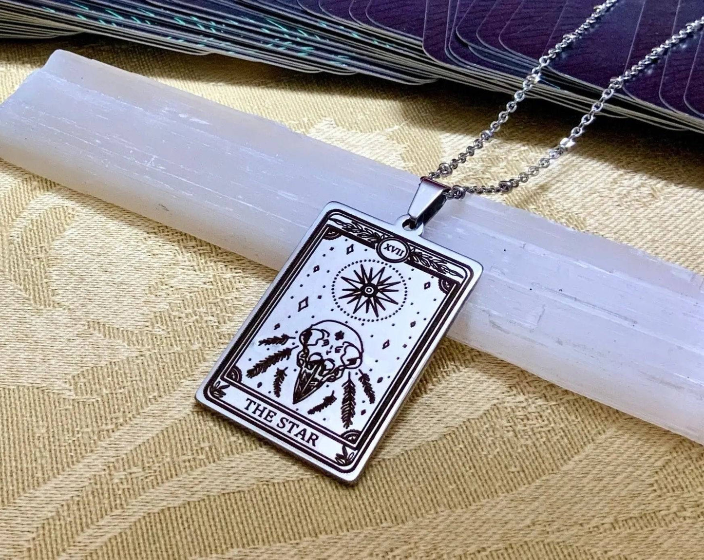 Close-up of The Star Tarot Card Necklace - 18k Gold featuring a skull and celestial design on a silver chain, laid on a selenite crystal.